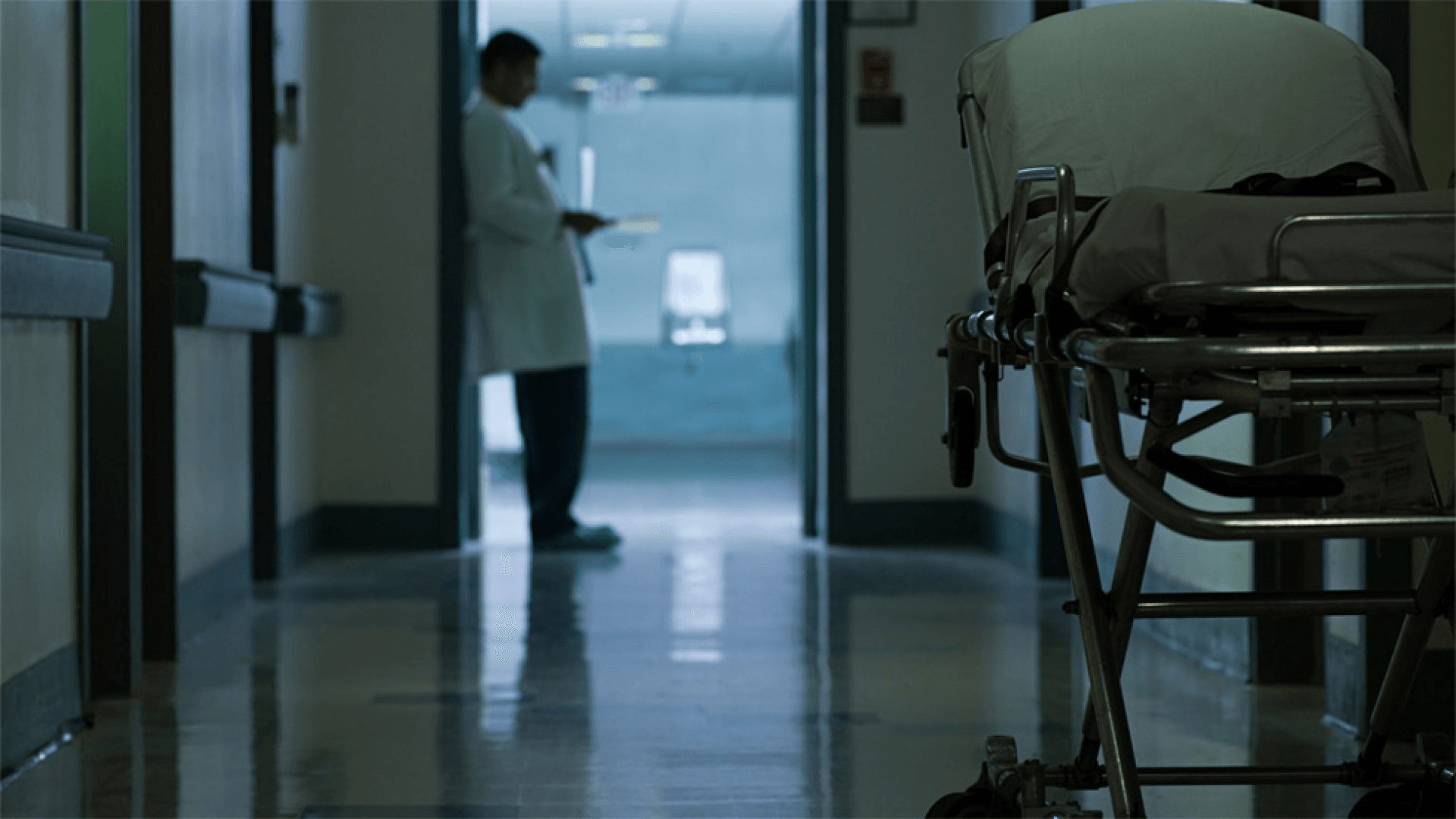 Turno di notte in ospedale: un medico guarda il cellulare in una corsia vuota.