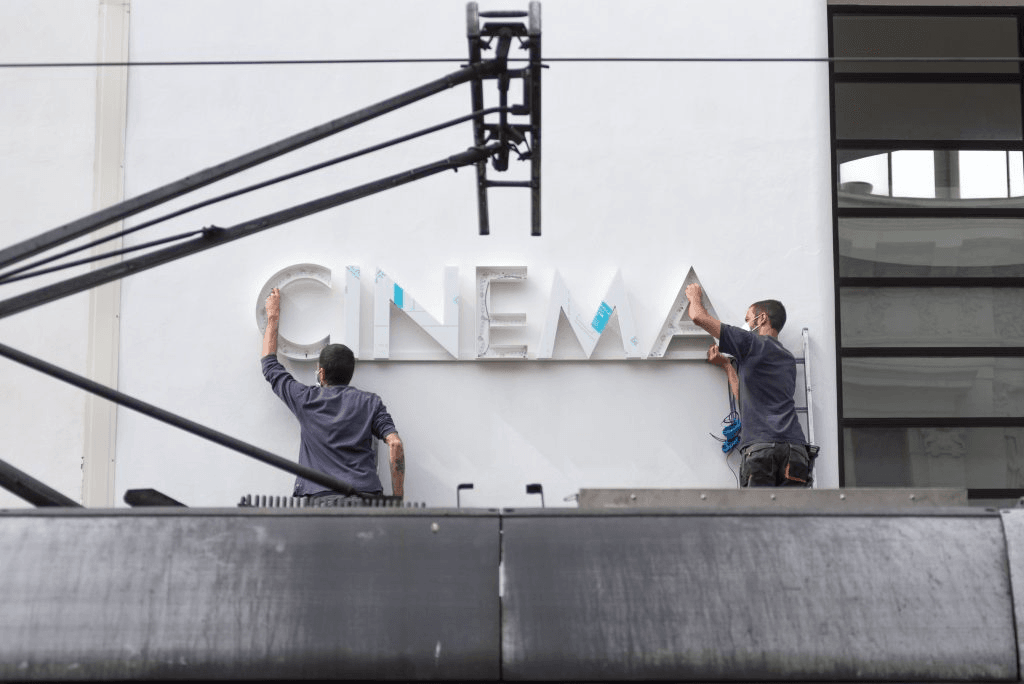 InSicurezza, il docufilm sugli incidenti sul lavoro: due operai riparano una scritta luminosa "cinema"