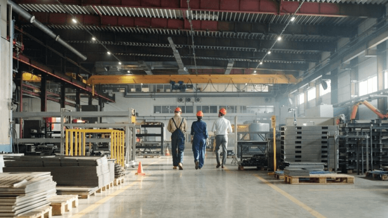Crisi in Lombardia: tre lavoratori di reparti diversi si allontanano nel capannone di un'industria