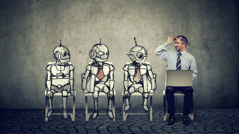 Quali competenze occorrono per gestire l'intelligenza artificiale? Un uomo osserva tre automi seduti accanto a lui, in abito di lavoro