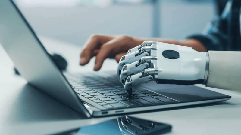 Intelligenza artificiale e risorse umane: una mano umana e una robotica scrivono sullo stesso PC
