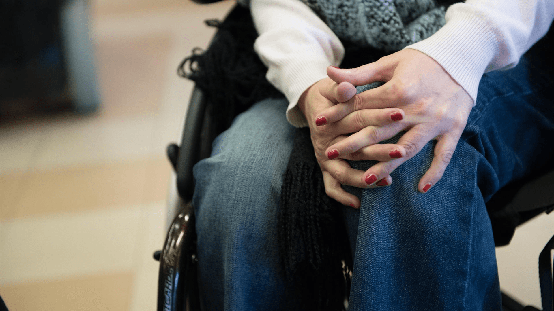 Donne, lavoro e disabilità: le mani di una ragazza in carrozzina incrociate sulle ginocchia
