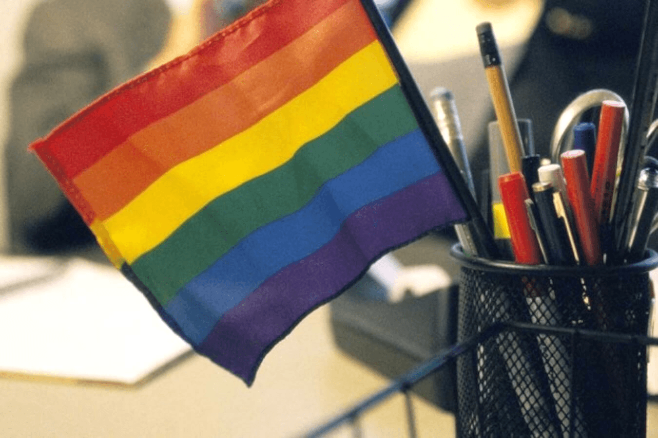 Discriminazioni per l'orientamento sessuale sul lavoro: una bandiera arcobaleno spunta dal portapenne su una scrivania