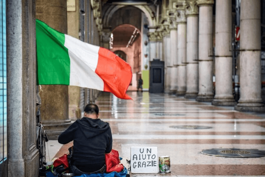 Povertà di stranieri e italiani: un clochard chiede l'elemosina con il tricolore a fianco