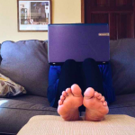 Rivoluzione coronavirus: un uomo lavora al portatile da casa, sul divano, a piedi nudi.