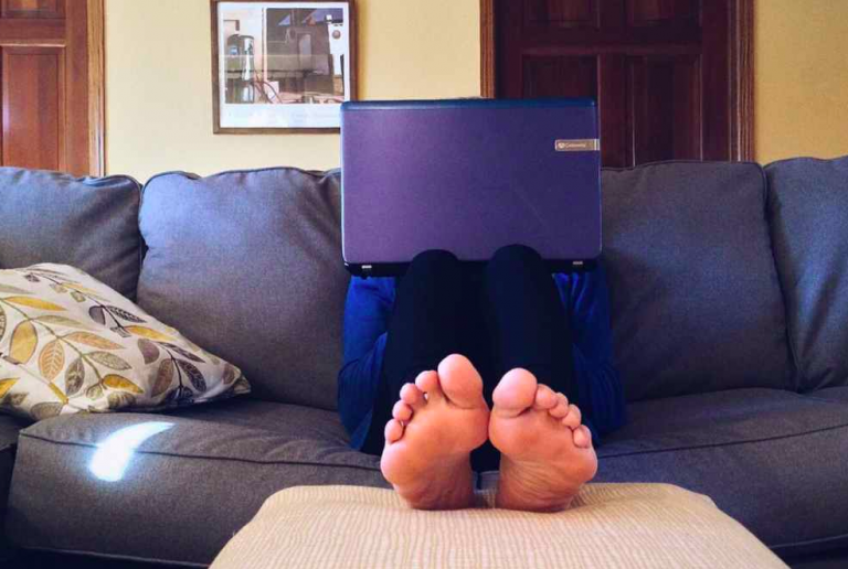 Rivoluzione coronavirus: un uomo lavora al portatile da casa, sul divano, a piedi nudi.