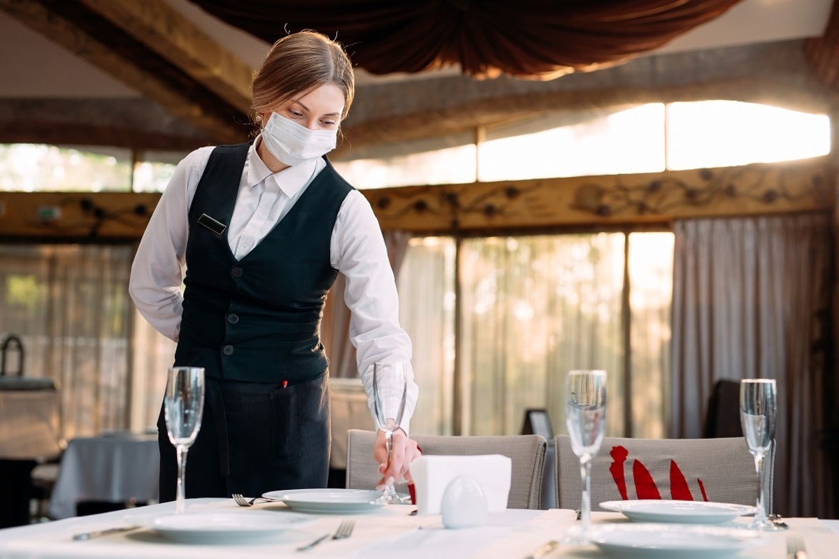 Ristorazione a Milano: una cameriera apparecchia un tavolo in mascherina in un ristorante di Milano