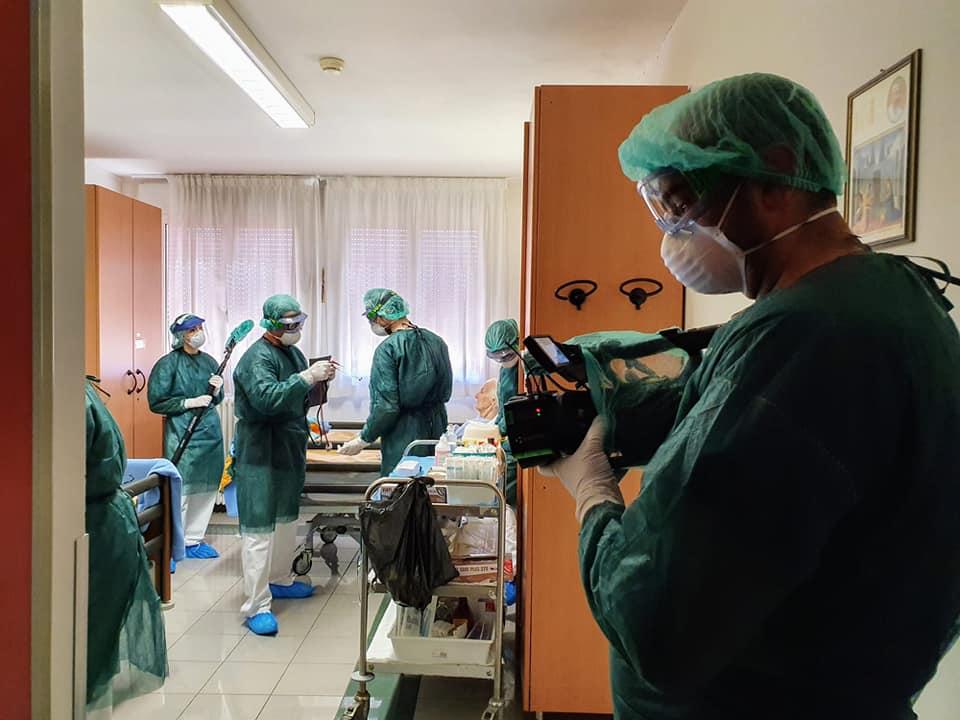 Un operatore effettua delle riprese in ospedale bardato con tuta, cuffia, guanti e mascherina.