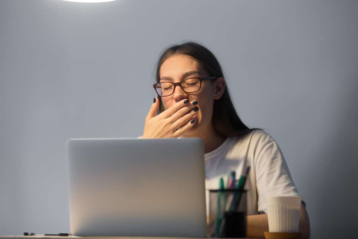 Una donna esausta sbadiglia davanti a un computer.