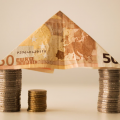 Salario minimo: un tetto composto da una banconota di 50 euro piegata e sostenuta da pile di monete.