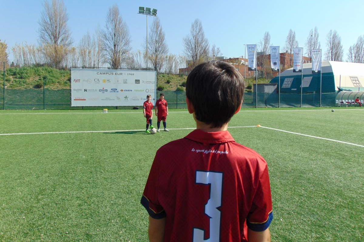 Un giovane calciatore osserva i suoi compagni da lontano.