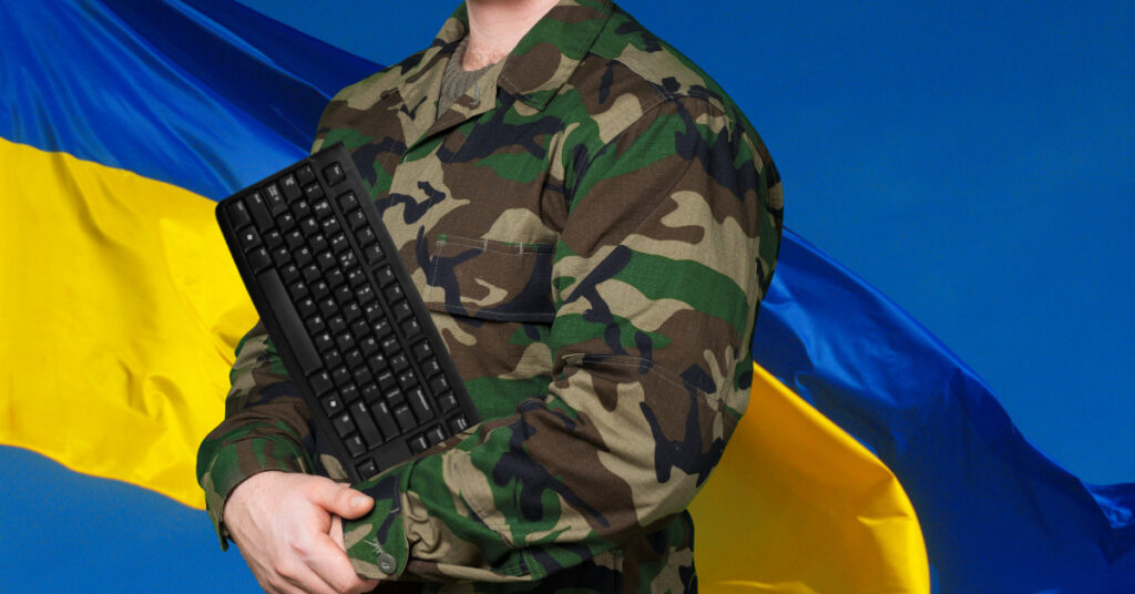 Ucraina, il lavoro IT non si ferma per la guerra: un soldato imbraccia una tastiera di fronte alla bandiera nazionale