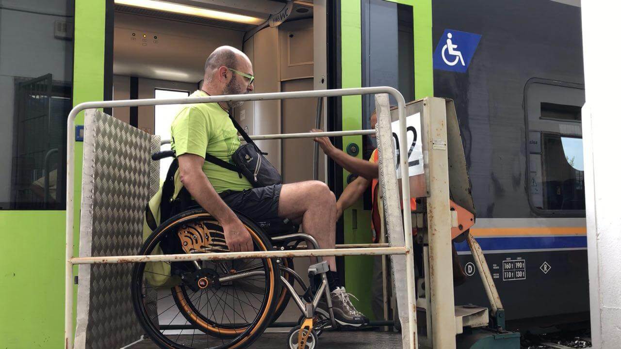 Accessibilità e disabilità, un uomo in carrozzina sale su un vecchio treno tramite una rampa