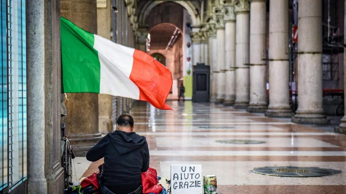 Stranieri e povertà in Italia: un immigrato chiede l'elemosina con a fianco la bandiera italiana.